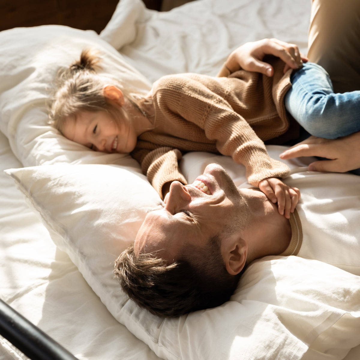 Father and daughter laughing and snuggling in bed on donated pillows