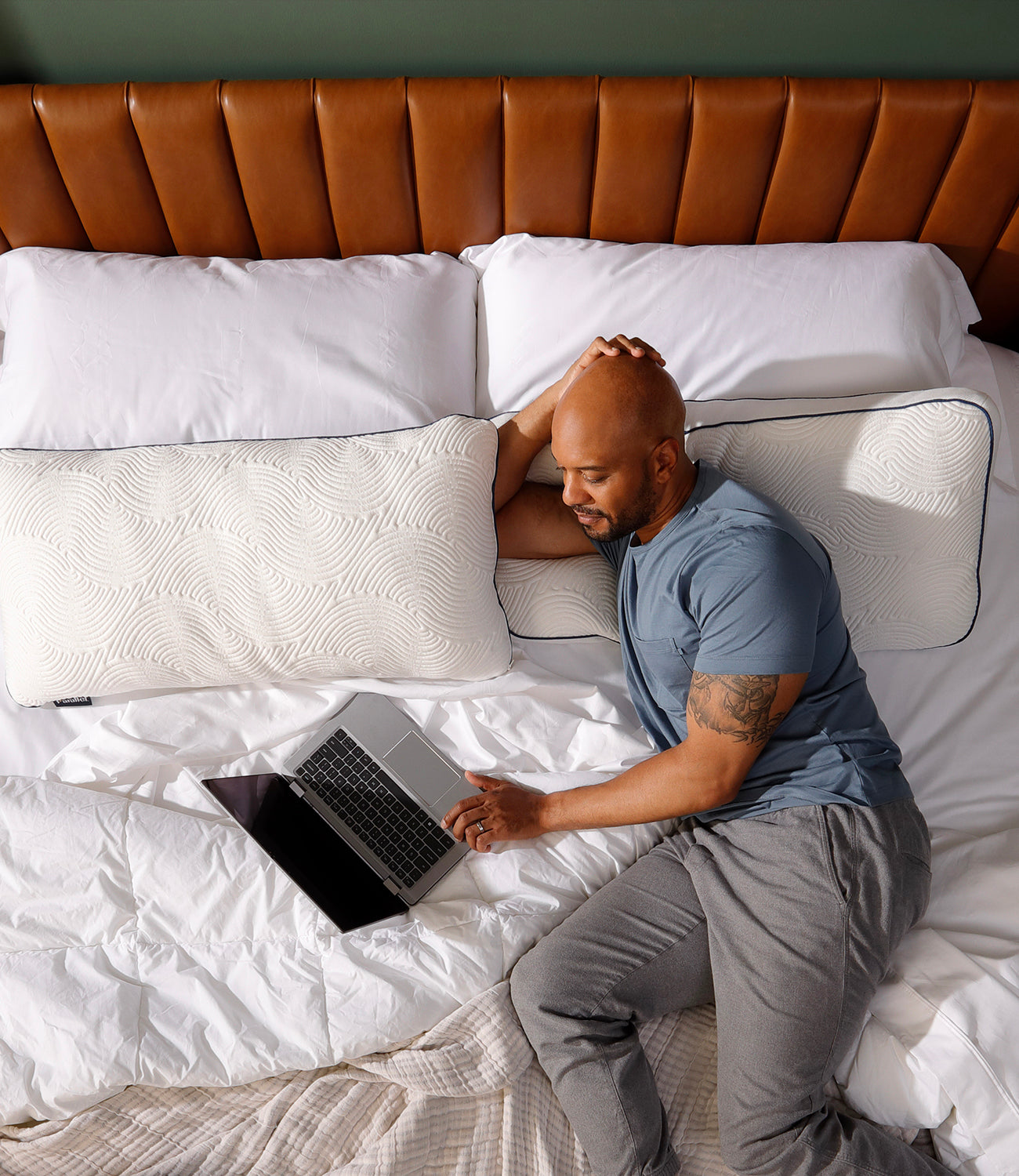 Man leaning on Parallel Pillow while using laptop in bed