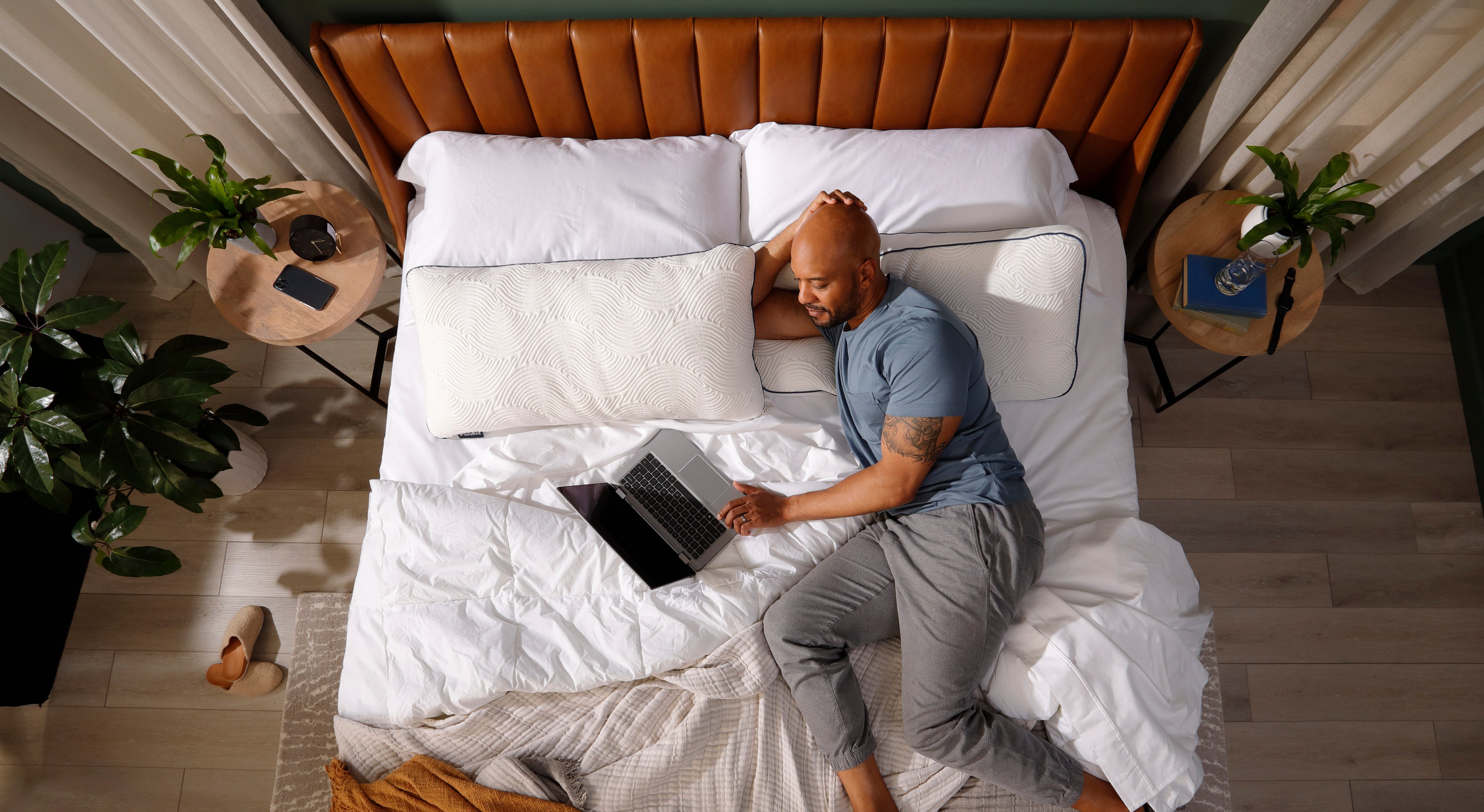 Man leaning on Parallel Pillow while using laptop in bed